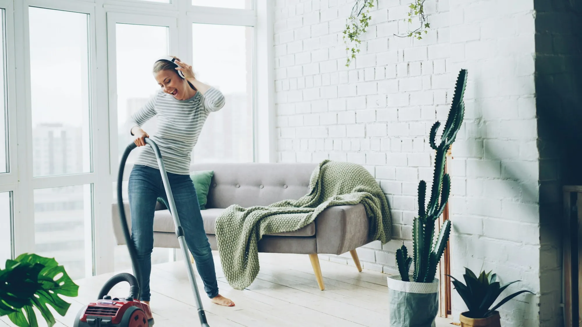 A cleaner vacuuming a bright, tidy living room with city views through floor to ceiling windows