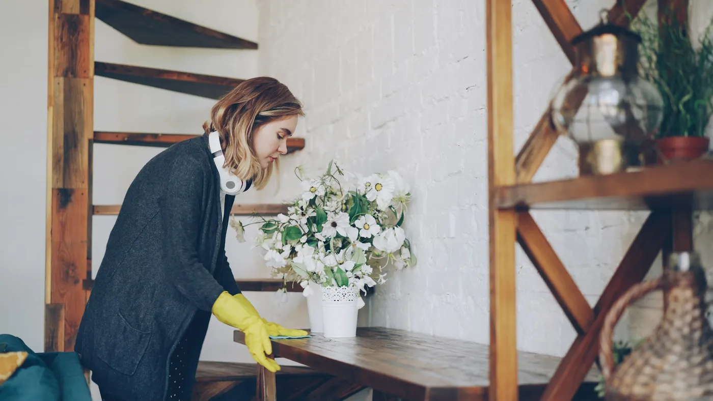 Hands in yellow gloves arranging flowers on a freshly wiped shelf